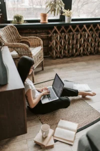 Girl sitting on the floor in the sitting room and applying for the Scholarship Owl Program on her laptop